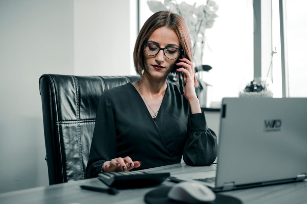 Businesswoman multitasking with a phone and calculator at a desk, showcasing office productivity.