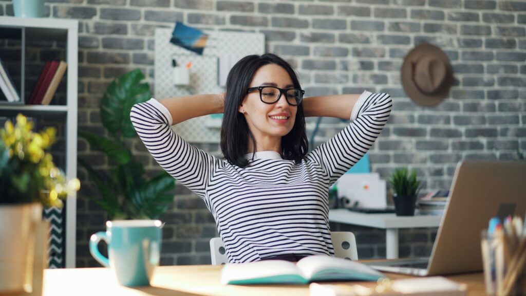Smiling woman in striped blouse relaxing at desk in a modern home office environment.