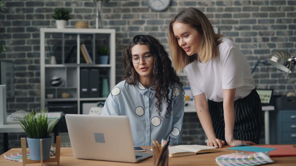 Two women working together on a laptop in a creative office space.